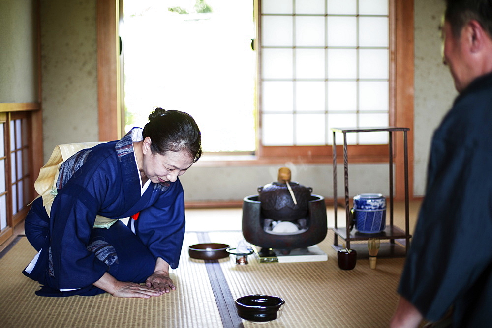 Japanese woman wearing traditional bright blue kimono with cream coloured obi and man kneeling on floor during tea ceremony, Kyushu, Japan