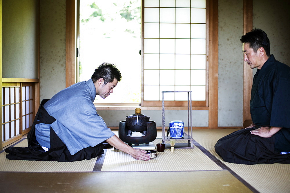 Two Japanese men wearing traditional kimonos kneeling on floor during tea ceremony, Kyushu, Japan