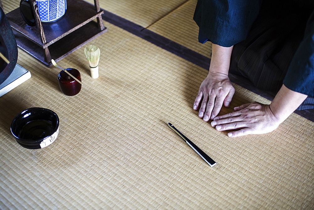 High angle close up of Japanese man kneeling on tatami mat in front of Sensu fan, bowl and whisk used in tea ceremony, Kyushu, Japan