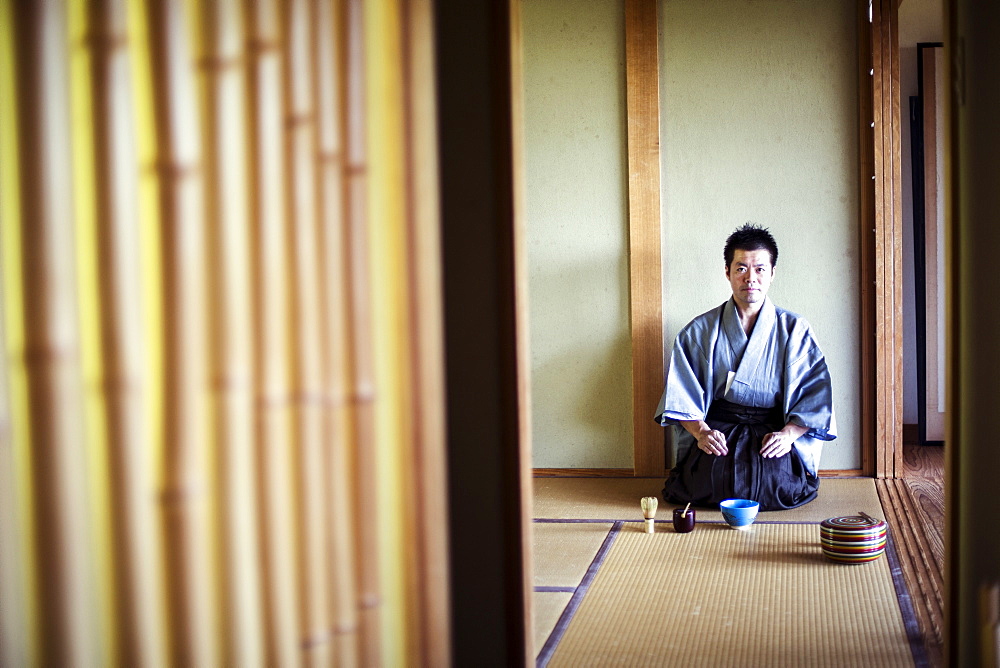 Japanese man wearing traditional kimono kneeling on tatami mat during tea ceremony, Kyushu, Japan