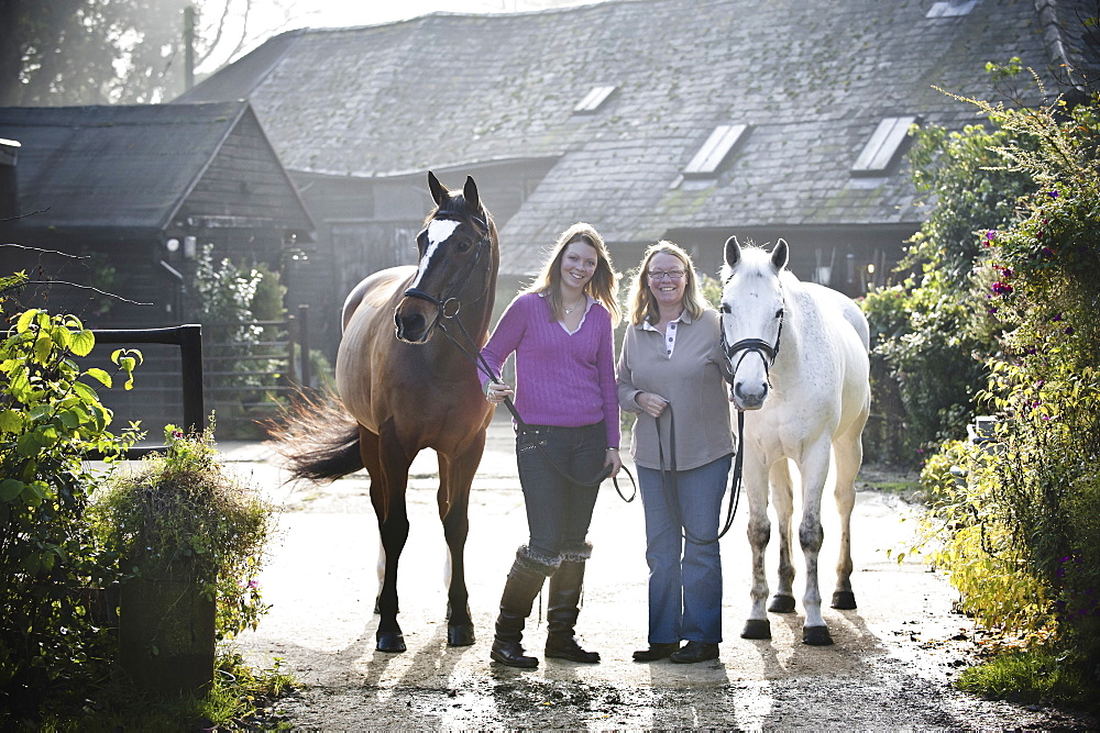 Two women standing outside a stable with two horses, England