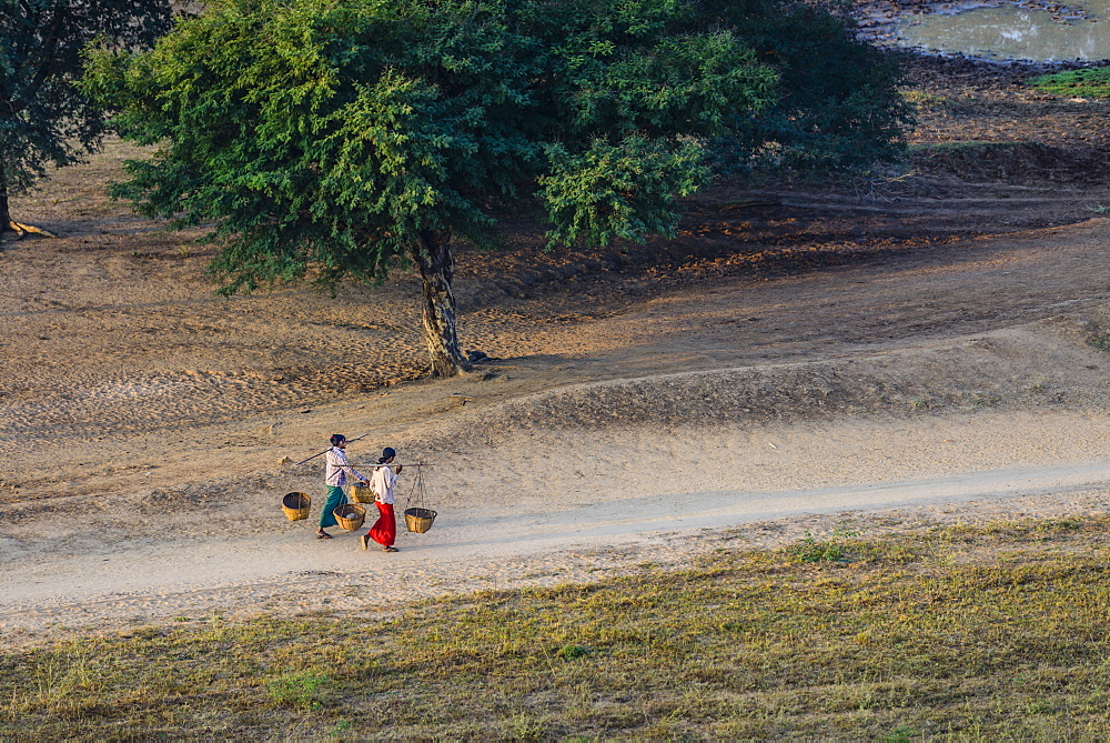 People carrying baskets on dirt path in rural landscape, Myanmar, Burma