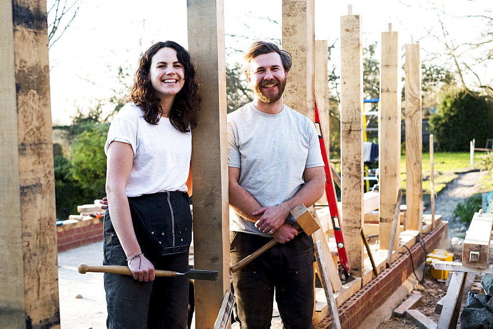 Smiling man and women holding hand tools standing on building site of residential building, Oxfordshire, England