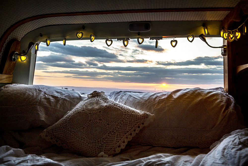 Camper van with cushion and fairy lights, view through rear window at sunset, Oxfordshire, England