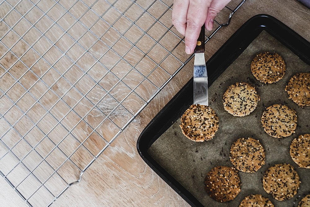 High angle close up of person removing freshly baked seeded crackers from a baking tray, England