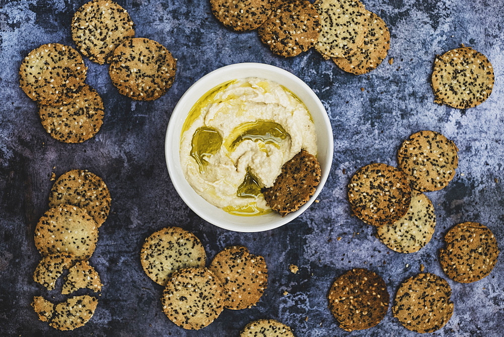 High angle close up of a bowl of hummus and freshly baked seeded crackers, England