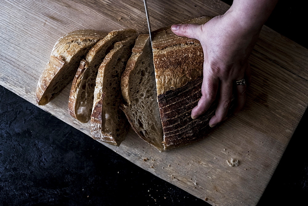 A hand holding a loaf of bread and using a breadknife to cut slices, England