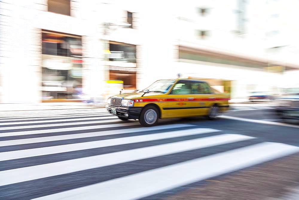 Motion blurred shot of yellow taxi cab on pedestrian crossing, Tokyo, Japan