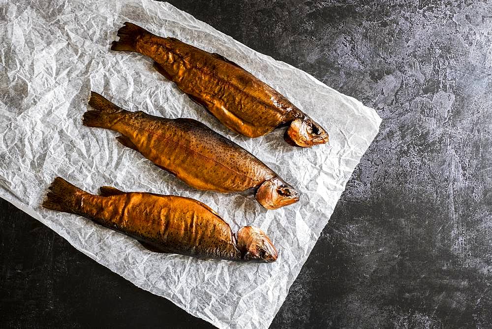 High angle close up of three freshly smoked whole trout on a white paper