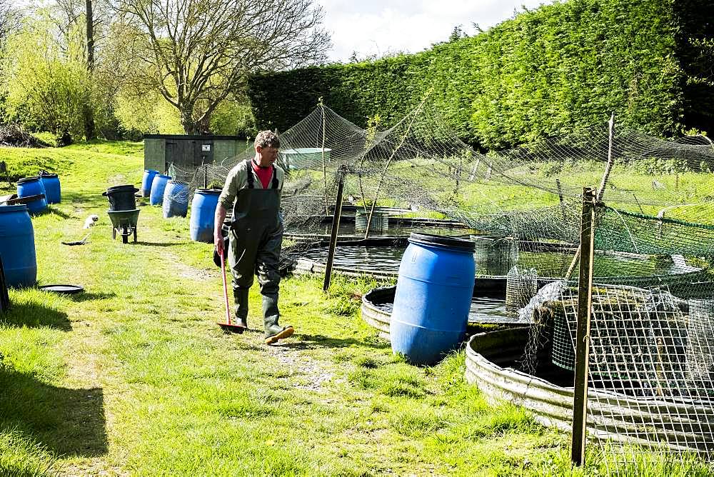 Man wearing waders walking past water tanks at a fish farm raising trout