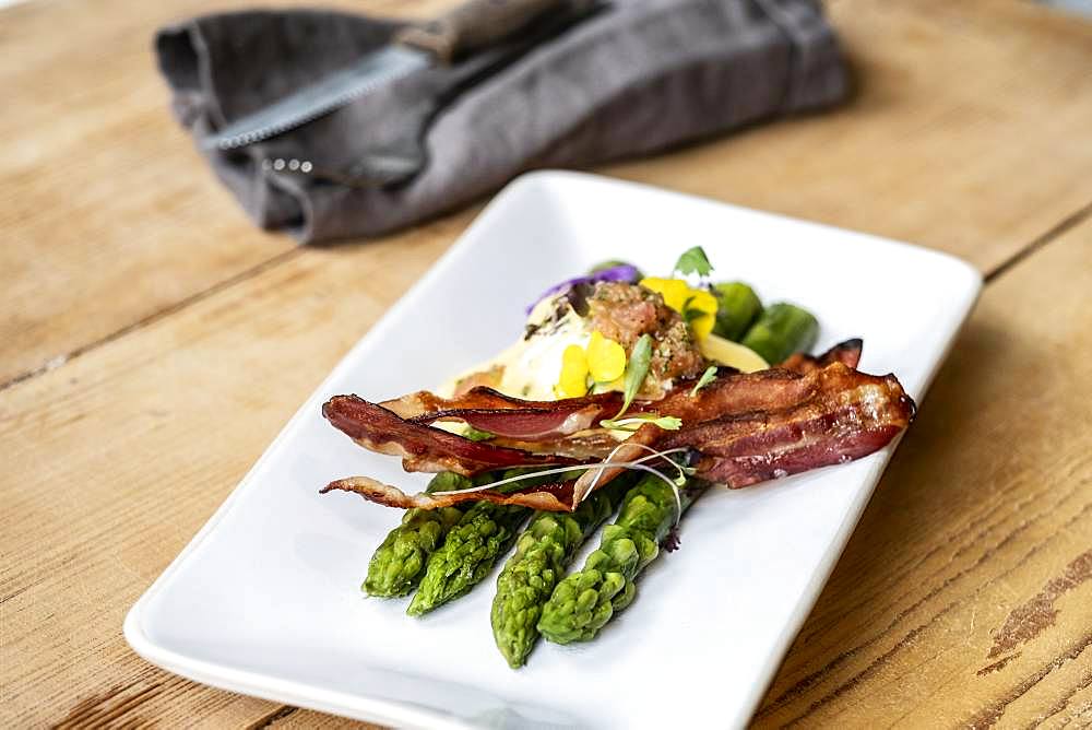 High angle close up of plate of green asparagus with crispy bacon and Hollandaise Sauce