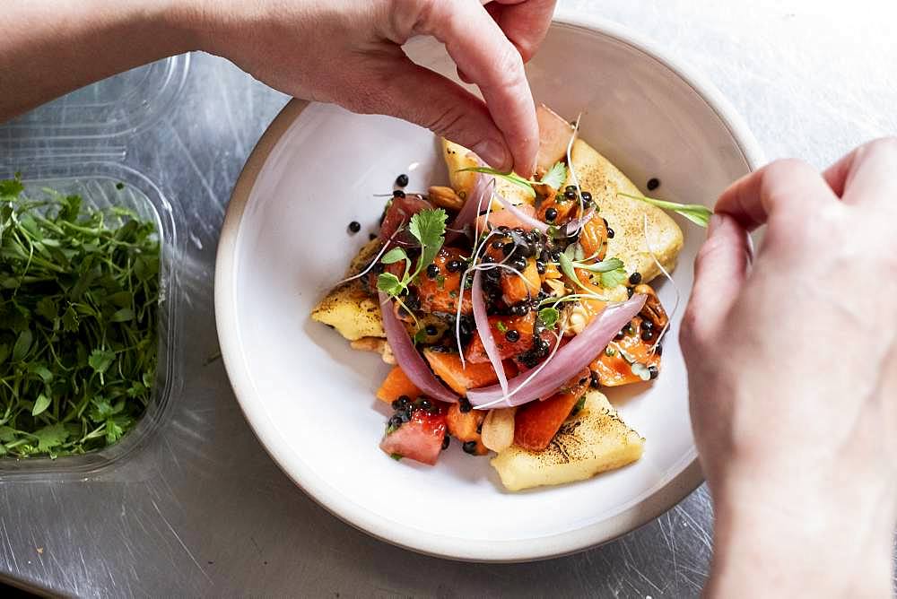 High angle close up of person garnishing plate of food with some herbs