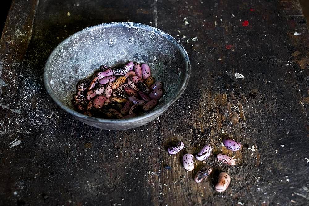 High angle close up of grey metal bowl with purple speckled beans on wooden table