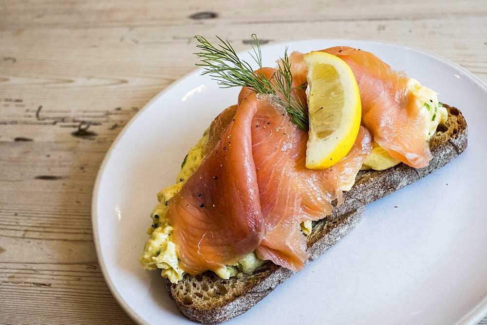 An open sandwich on rye bread with a topping of cured salmon or fish with garnish of a slice of lemon