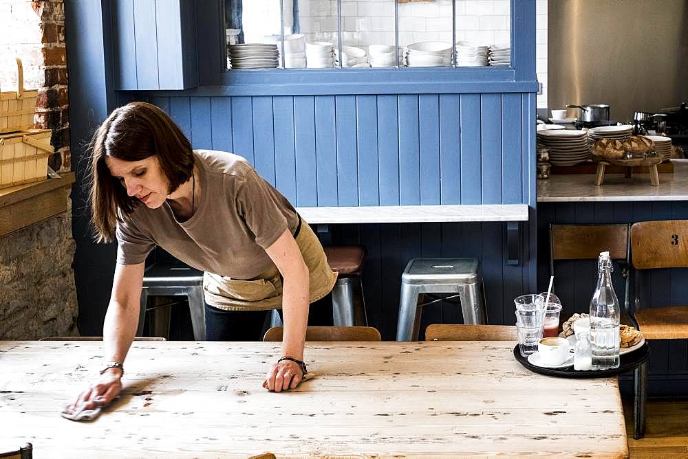 A female waitress clearing a table and wiping it in a cafe