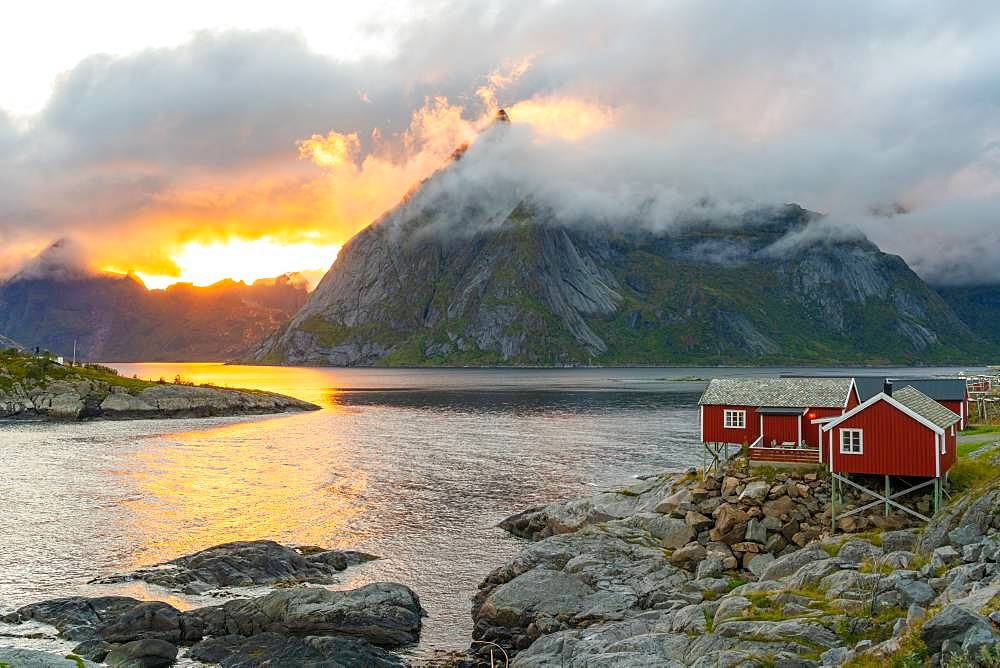 Low clouds swirling round and covering the mountains, a small traditional rorbu house on the shoreline Lofoten Islands, Norway