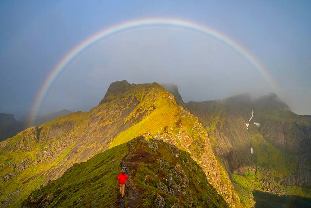 Man climbing towards a rainbow in the Lofoten Islands, Norway