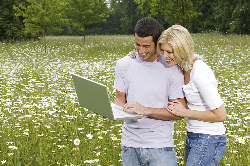 A man and woman in a flower meadow, looking at a laptop screen, England