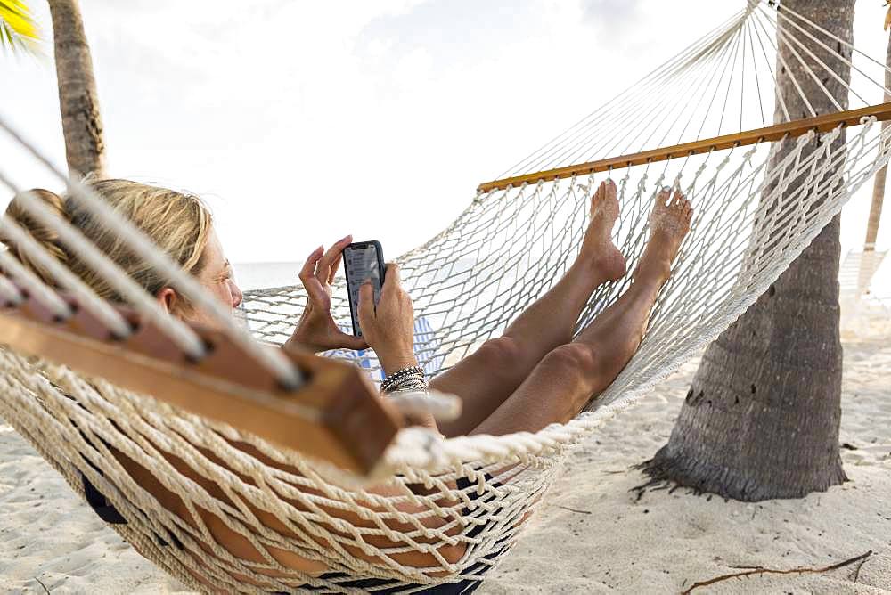 Woman in hammock using her smart phone, Grand Cayman, Cayman Islands