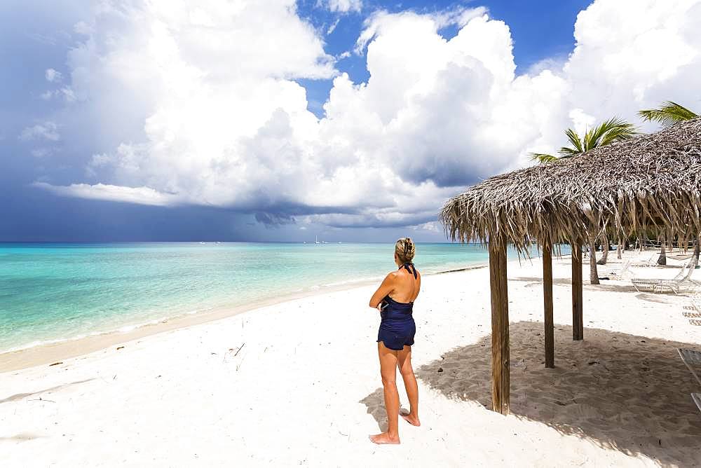 Adult woman watching approaching storm clouds from a beach, Grand Cayman, Cayman Islands