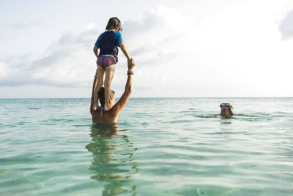 5 year old son on mother's shoulders leaping into the ocean at sunset, Grand Cayman, Cayman Islands