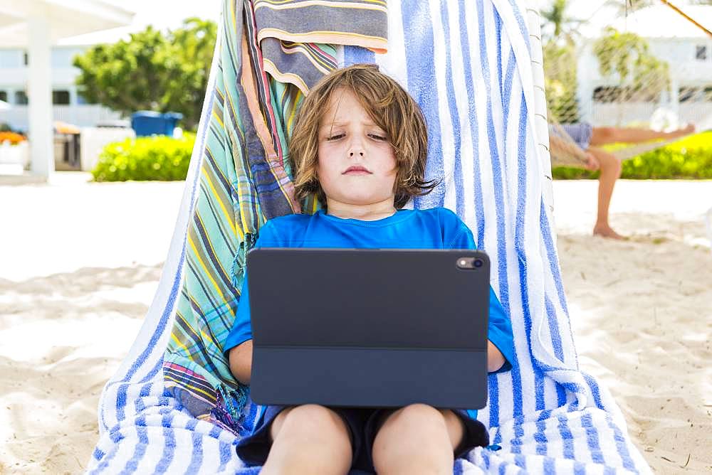 5 year old boy using laptop at the beach, Grand Cayman, Cayman Islands