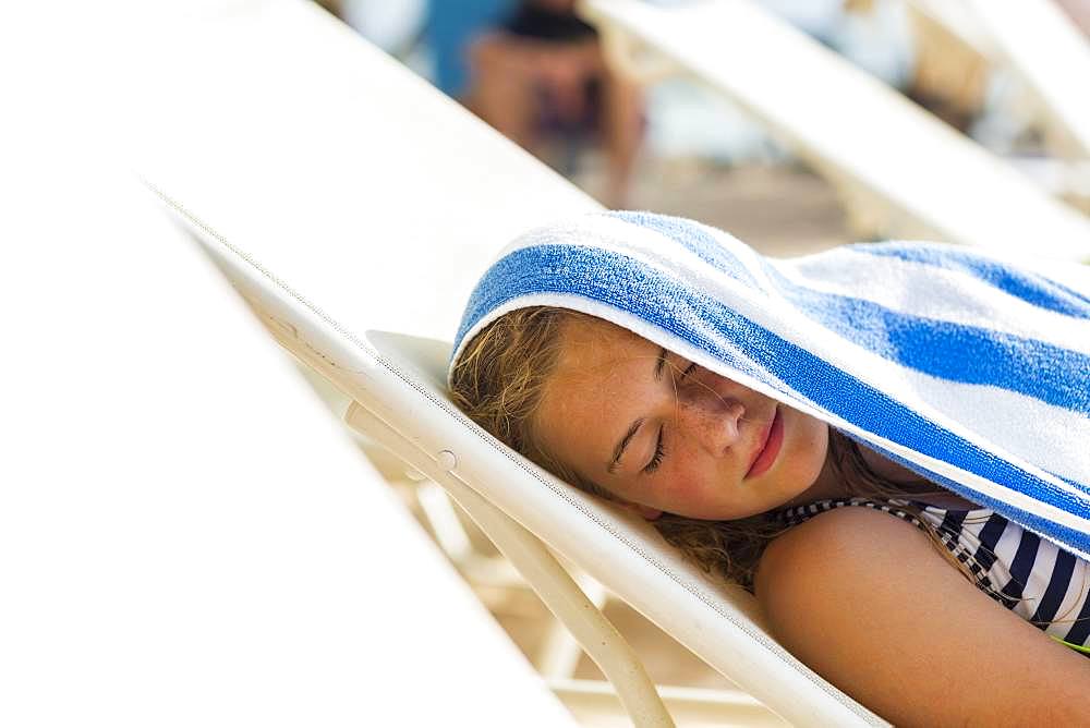 A teenage girl reclining in beach chair with towel on her head, Grand Cayman, Cayman Islands