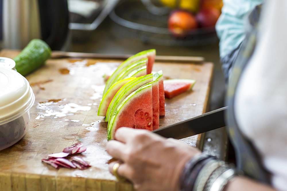 close up of hands cutting watermelon slices in kitchen