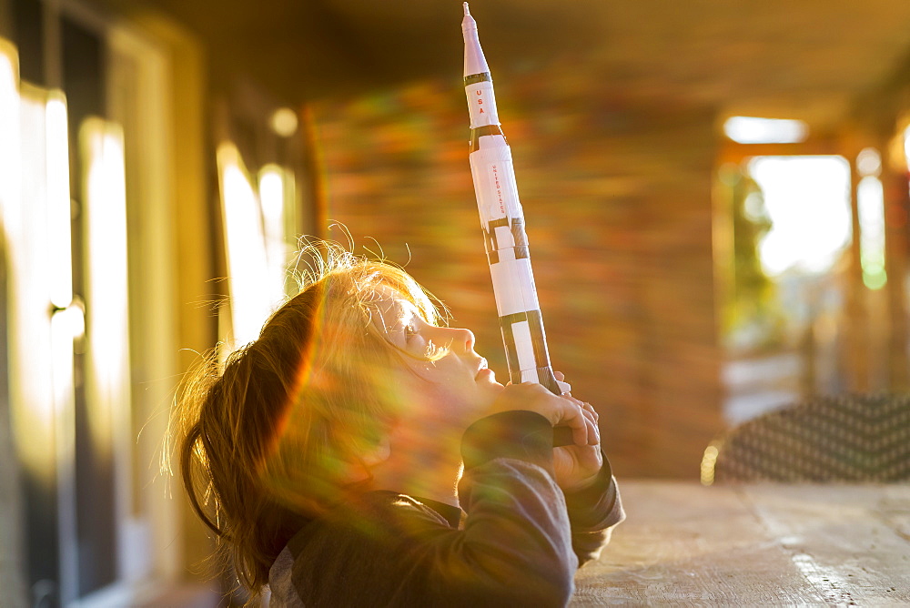 A boy playing with a toy Nasa Saturn 5 rocket, day dreaming about space flight