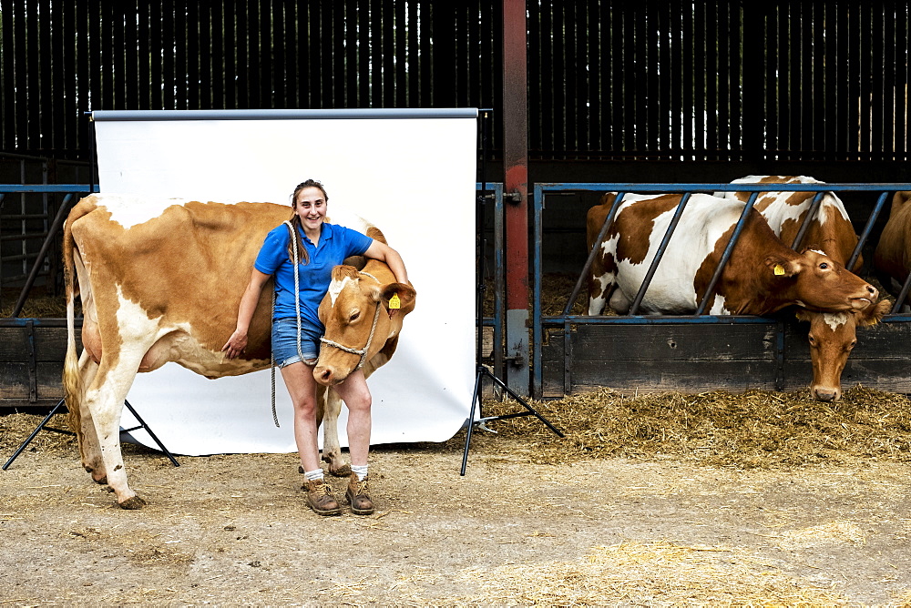 Portrait of female farmer standing in front of a barn with a Guernsey cow