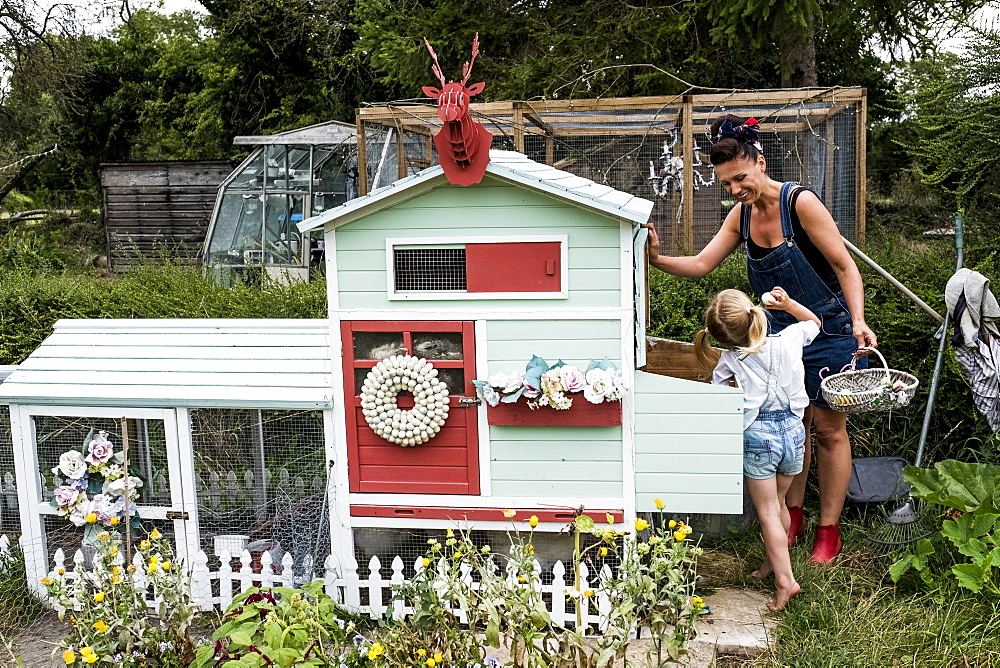 Smiling woman and girl standing in a garden next to a colourful hen house