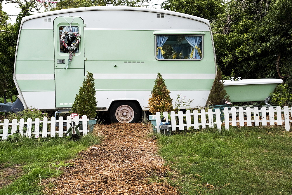 White and green retro caravan parked at the end of a garden path behind low white picket fence