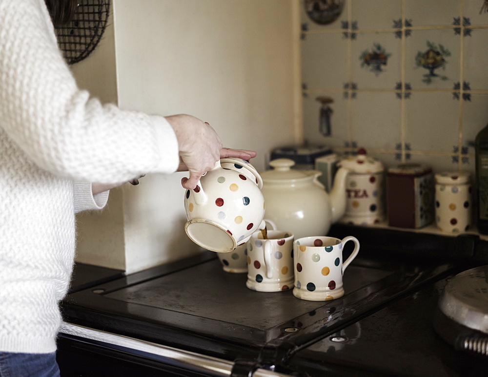 A woman pouring tea, by a range cooker. Using decorative china, Ringwood, Hampshire, England