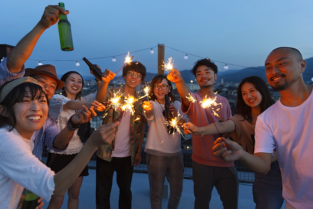 Group of young Japanese men and women with sparklers on a rooftop in an urban setting, Fukuoka, Kyushu, Japan