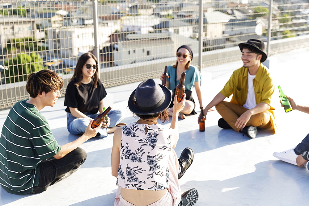 Smiling group of young Japanese men and women sitting on a rooftop in an urban setting, Fukuoka, Kyushu, Japan