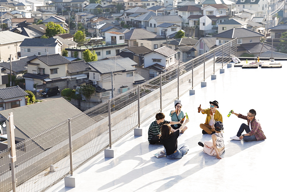 High angle view of group of young Japanese men and women sitting on a rooftop in an urban setting, Fukuoka, Kyushu, Japan