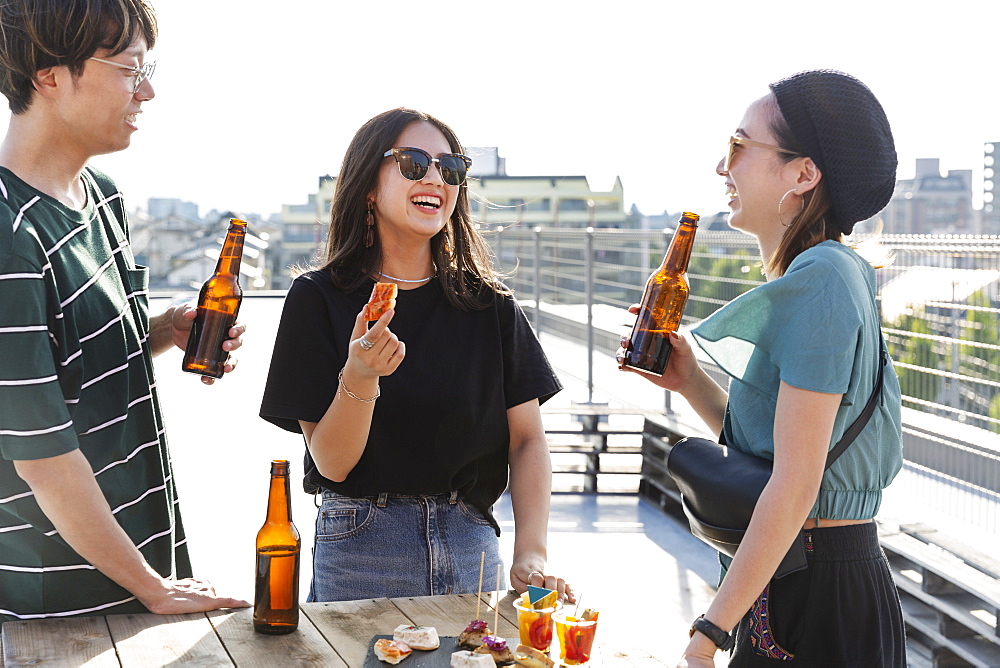 Young Japanese man and two women standing on a rooftop in an urban setting, drinking beer, Fukuoka, Kyushu, Japan