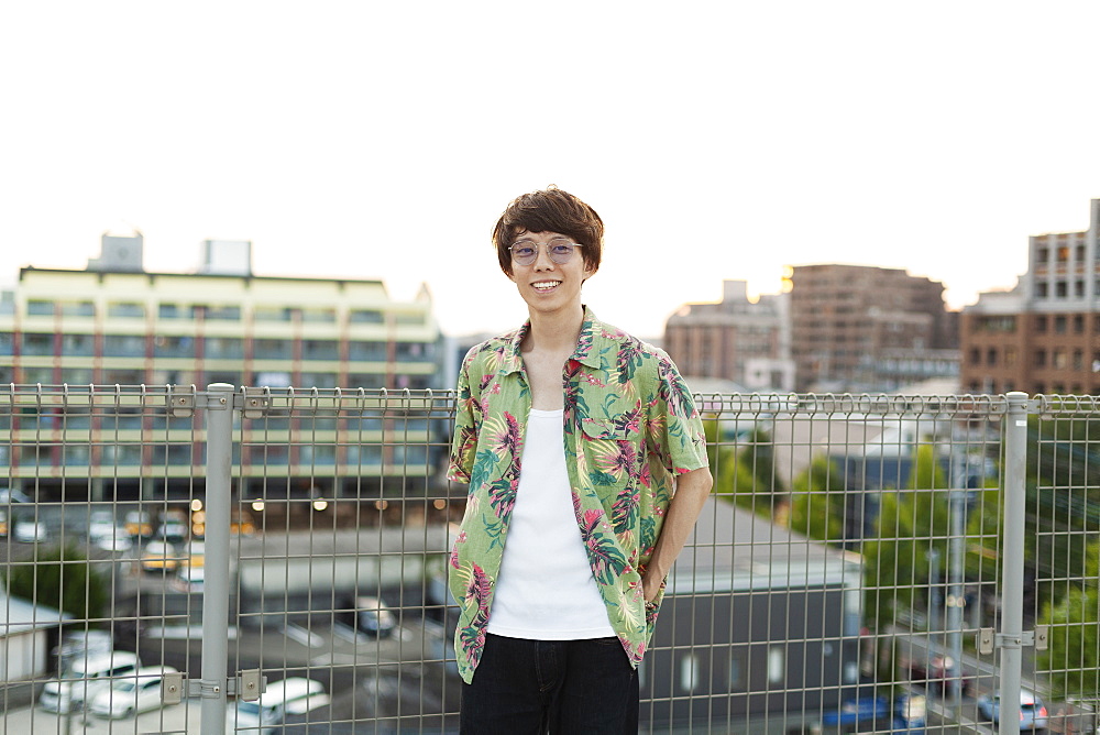 Young Japanese man standing on a rooftop in an urban setting, looking at camera, Fukuoka, Kyushu, Japan