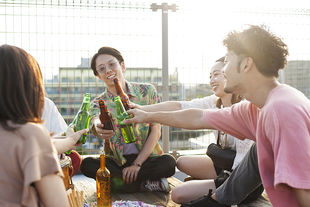 Group of young Japanese men and women sitting on a rooftop in an urban setting, drinking beer, Fukuoka, Kyushu, Japan