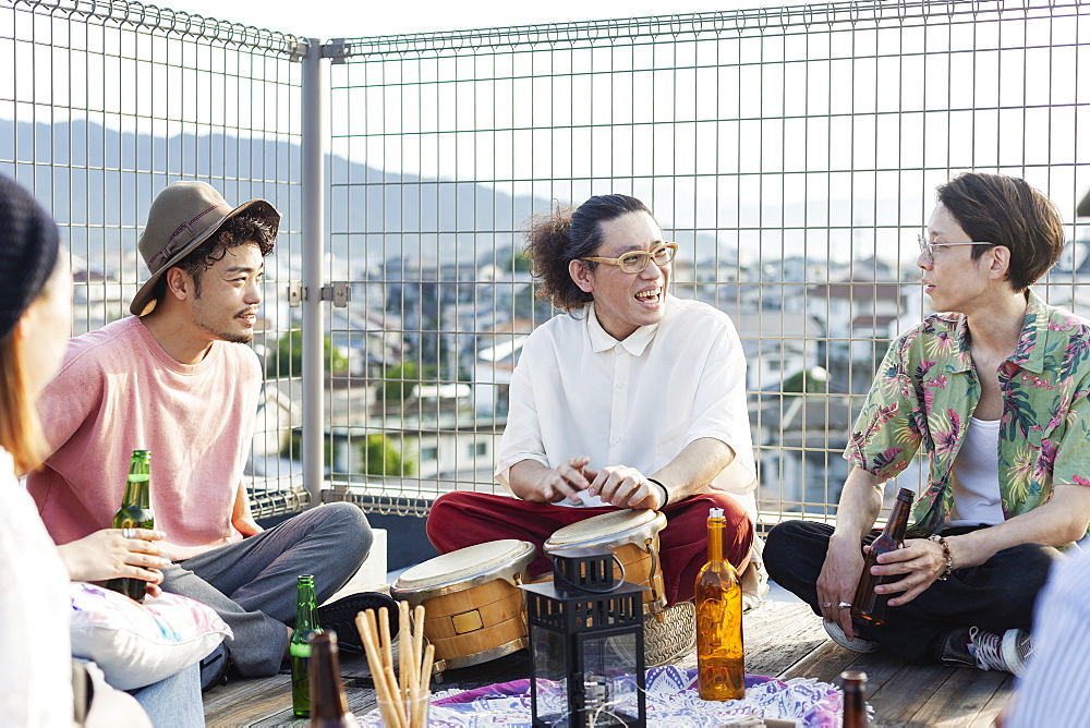 Group of young Japanese men and women sitting on a rooftop in an urban setting, drinking beer, Fukuoka, Kyushu, Japan