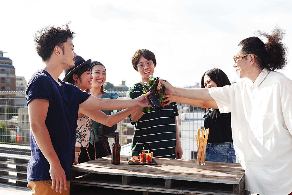 Group of young Japanese men and women standing on a rooftop in an urban setting, drinking beer, Fukuoka, Kyushu, Japan