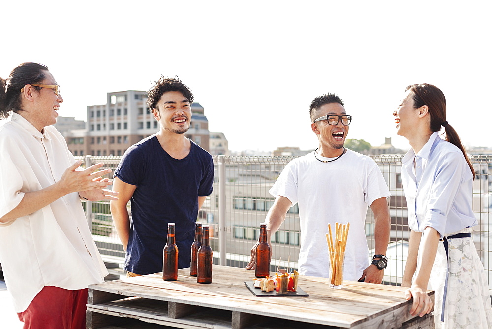 Group of young Japanese men and women standing on a rooftop in an urban setting, drinking beer, Kyushu, Japan