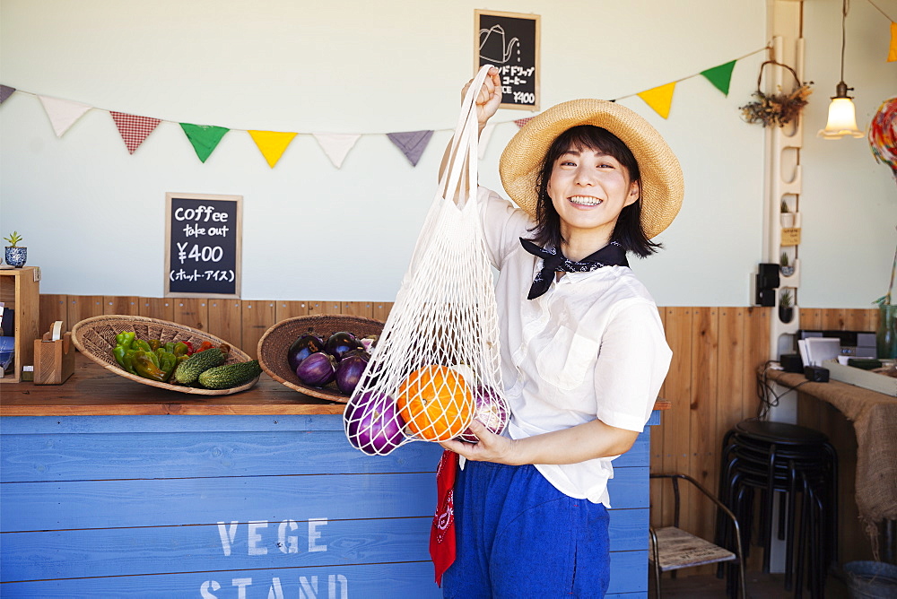 Japanese woman wearing hat working in a farm shop, smiling at camera, Kyushu, Japan