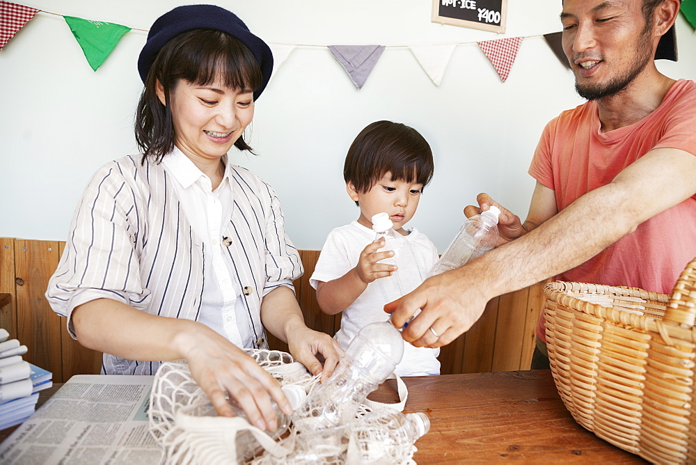 Japanese man, woman and boy standing in a farm shop, sorting clear plastic bottles into basket, Kyushu, Japan