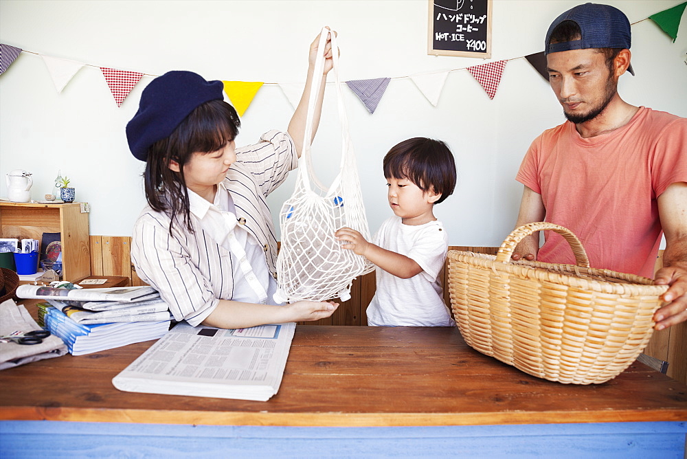 Japanese man, woman and boy standing in a farm shop, sorting clear plastic bottles into basket, Kyushu, Japan