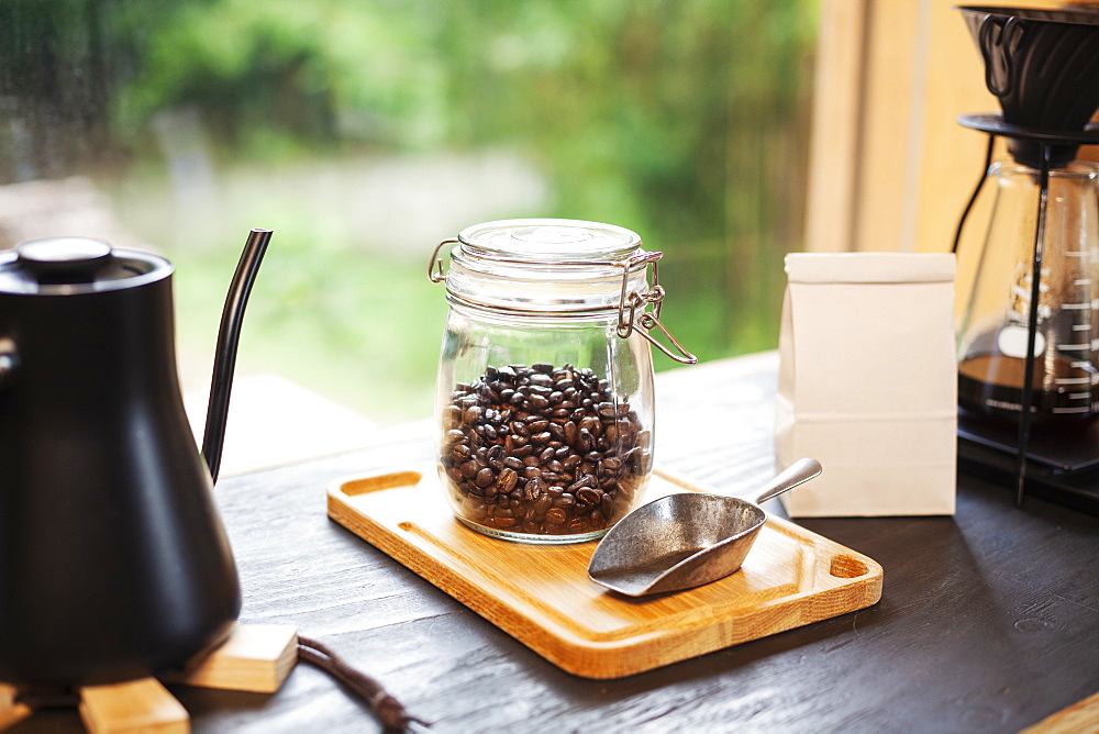 Close up of coffee pot, glass jar with coffee beans and metal coffee shovel on wooden board, Kyushu, Japan