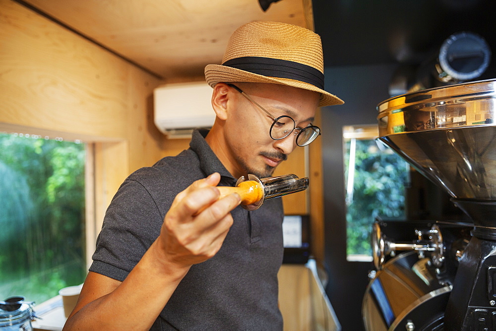 Japanese man wearing hat and glasses standing in an Eco Cafe, smelling freshly roasted coffee beans, Kyushu, Japan