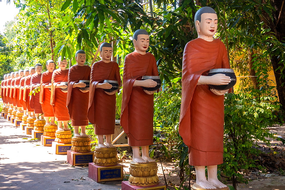 Row of Buddhist monk statues with red robes and alms bowls in the gardens of the Buddhist Temple at Siem Reap, Cambodia