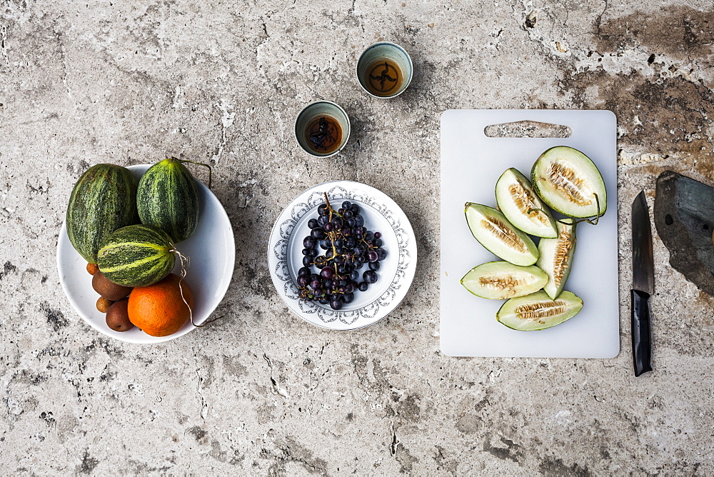 High angle close up of a stone table, with tea and selection of fresh fruits on plates and cutting board, China