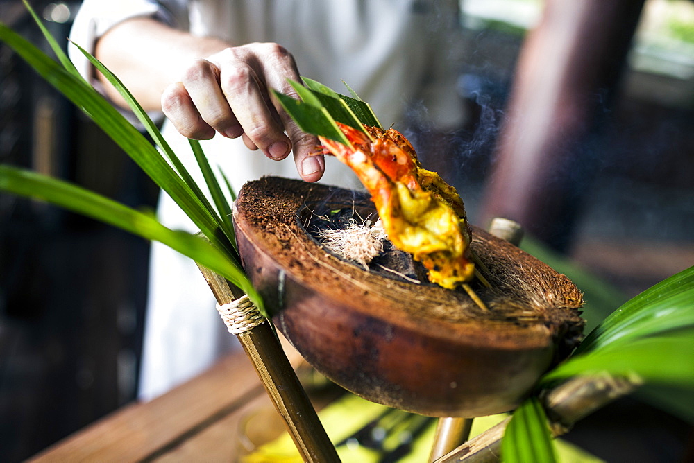 Close up of chef preparing charcoal-grilled prawn satay on a coconut shell, Thailand